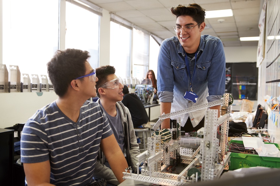 Teacher With Two Male College Students Building Machine In Science Robotics Or Engineering Class