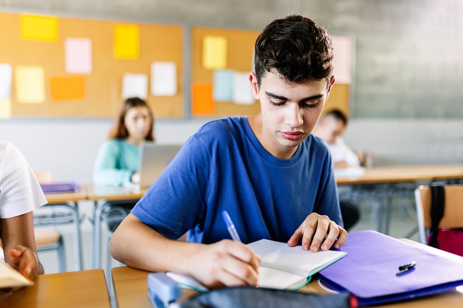 High school young student writing on notebook in class - Teenage boy sitting at desk doing exercise in classroom