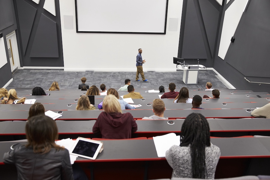 Man lectures students in lecture theatre, back row seat POV