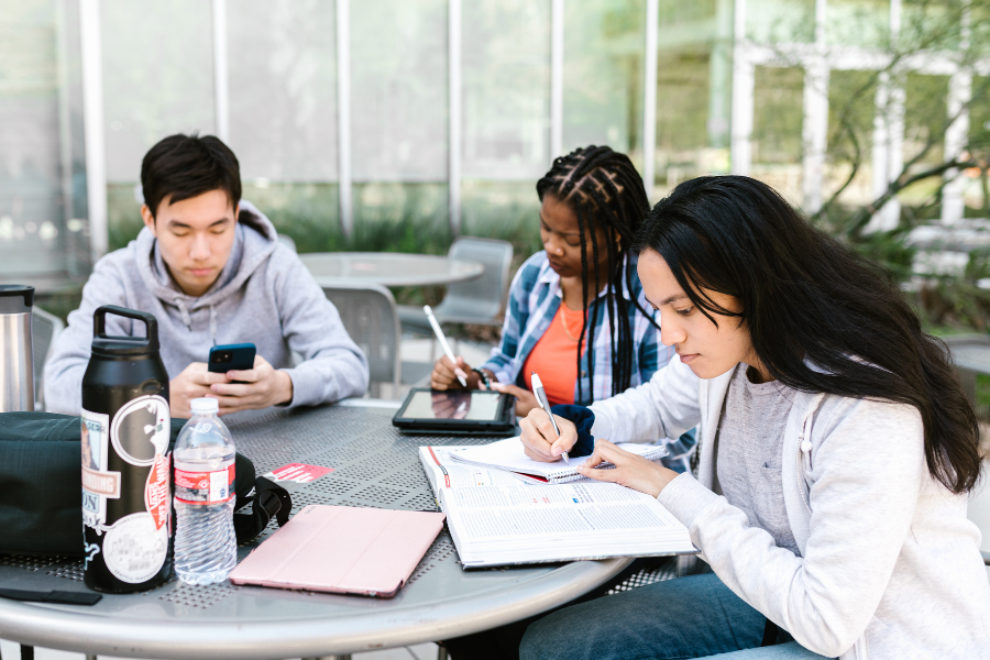 Three college students studying and collaborating outdoors on campus, representing the process of earning and transferring credits between colleges