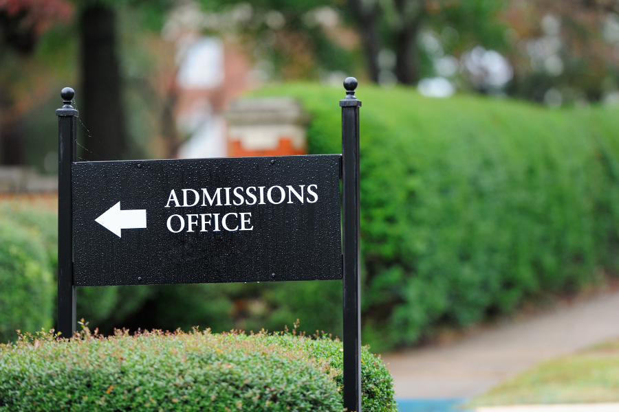 College admissions office sign on campus with green bushes in the background