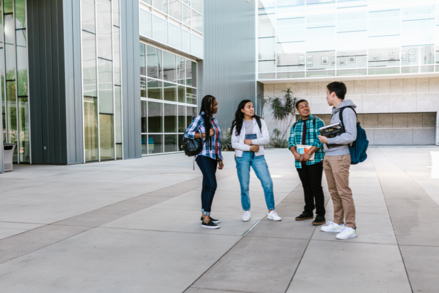 Group of diverse college students standing and talking on a modern campus, representing the collaborative and diverse environment of college life.