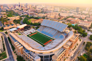 Aerial view of the University of Texas at Austin's football stadium, surrounded by campus buildings and the city skyline at sunset.