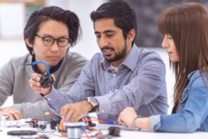 Three students working collaboratively on an engineering project, assembling components and discussing ideas in a classroom setting.