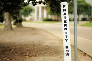 A white post labeled "Fraternity Row" on a college campus, symbolizing Greek life and student organizations in higher education.